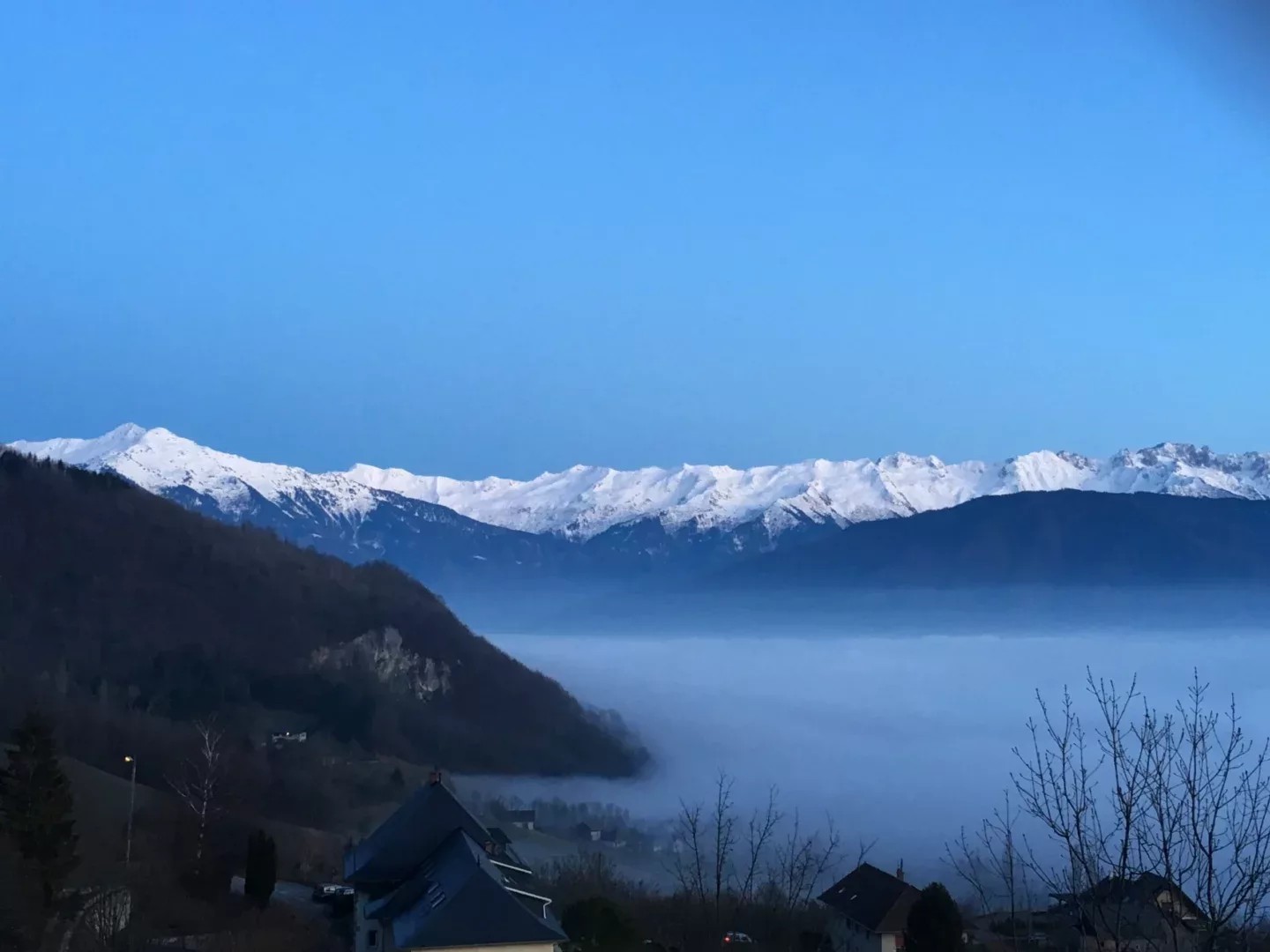 Vue de montagnes enneigées sous un ciel bleu avec du brouillard dans la vallée.