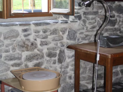 Tour de potier beige installé sur un support avec un éclairage et une table à proximité.