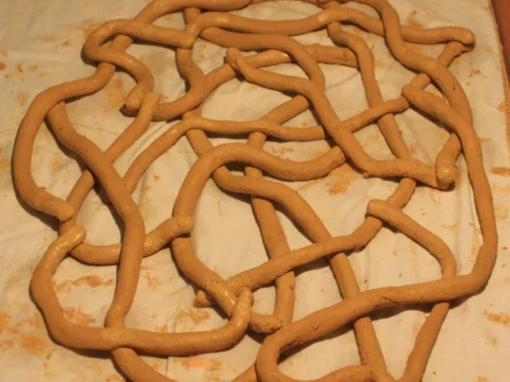 Sculpture en argile de couleur beige formant un motif enchevêtré sur une surface claire.