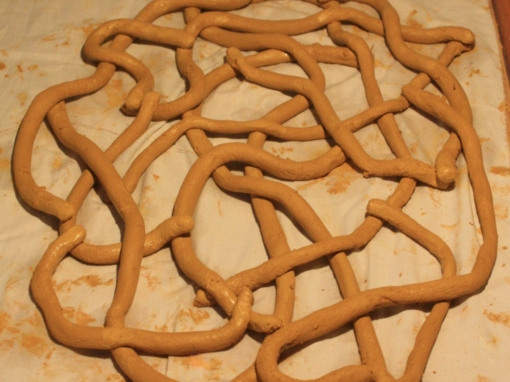 Sculpture en argile de couleur beige formant un motif enchevêtré sur une surface claire.