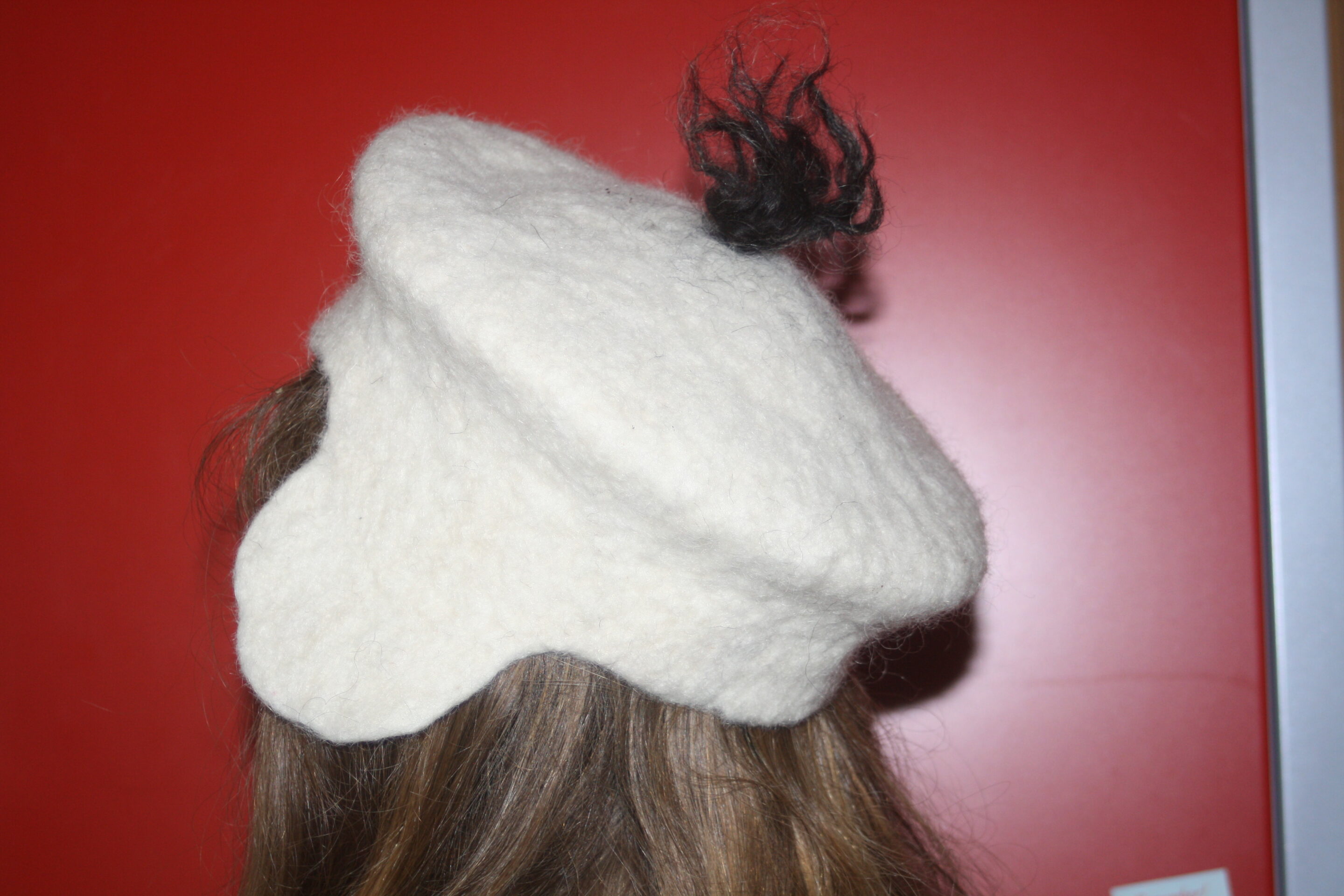 Chapeau en feutre blanc vu de profil, avec un pompon noir sur le dessus.