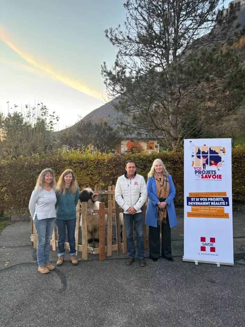 Groupe de quatre personnes lors de l’inauguration de l’association Les Fées Noumenes à Fréterive, posant près d’une bannière « Vos Projets pour la Savoie » et d’un cadre en bois.